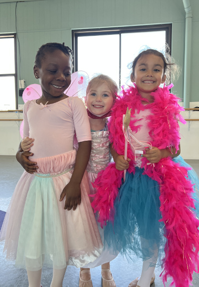 Metrowest Dance Academy "At the Theater" summer program. Three dance students ages 4 to 7, laughing and dressing up with sparkly clothes, fairy wings and feather boa.