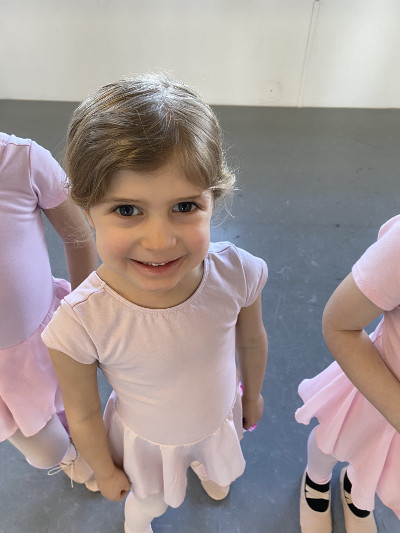 Young student in cute pink dress smiling at the camera, ready for "Little Steps" dance class, age 3 to 5. Metrowest Dance Academy.