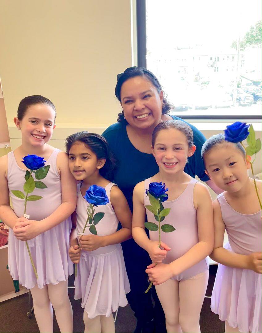 Four young students in pink, holding blue roses, photographed with their instructor at their primary RAD exam.