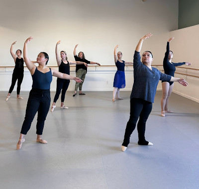 Group of adult dancers learning positions in bright spacious studio.