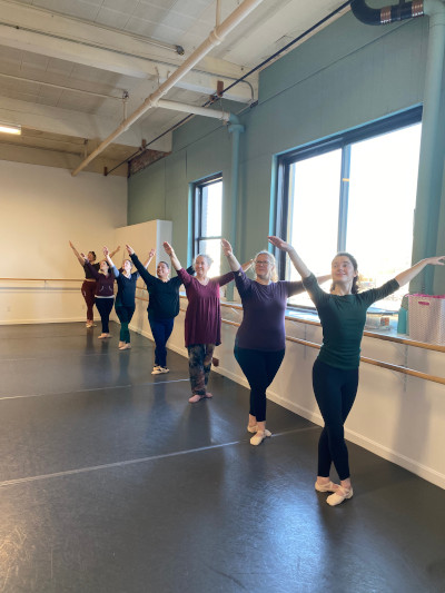 Group of adult dancers practicing poses at the barre.
