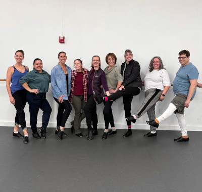 Group of participants in the tap dance classes, in a line and kicking out with tap shoes.